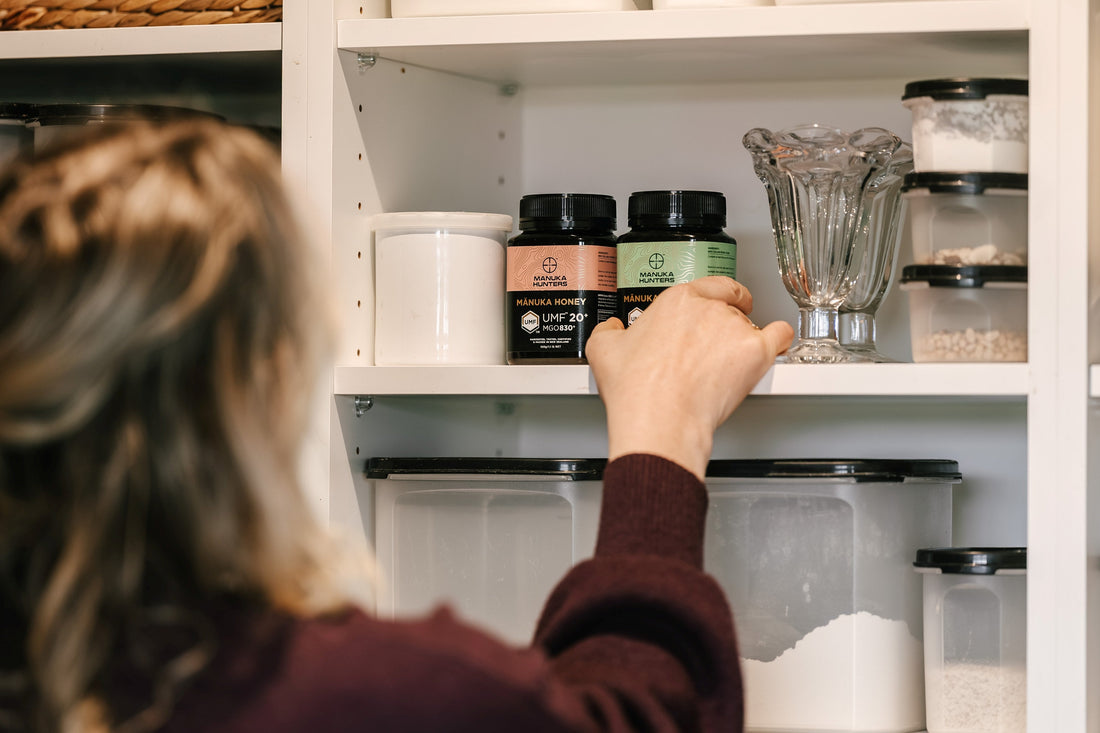 a woman choosing a jar of manuka hunters honey from a kitchen shelf