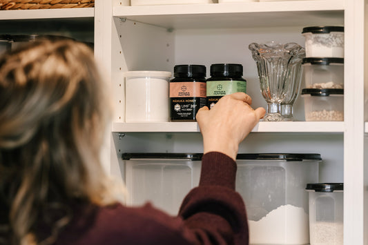 a woman choosing a jar of manuka hunters honey from a kitchen shelf
